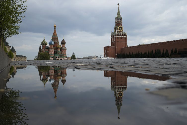 the Kremlin's Spasskaya Tower and St. Basil's Cathedral reflected in rain water puddles in Red Square in Moscow, Russia