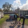 A couple plays with their dogs at a Louisiana home with a refinery in the background.