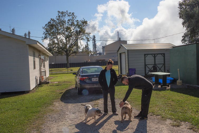 A couple plays with their dogs at a Louisiana home with a refinery in the background.