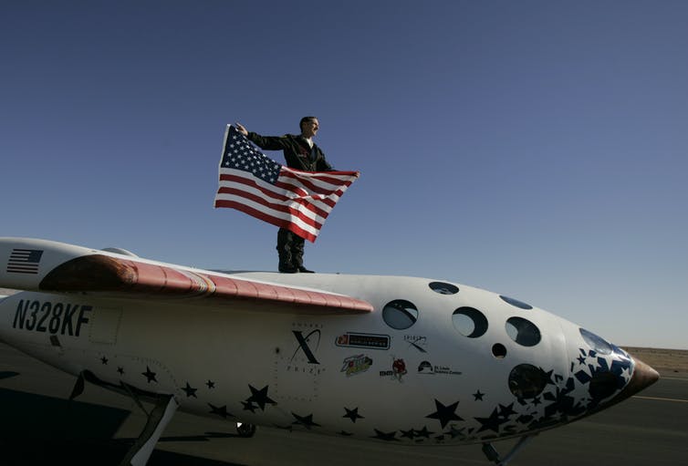 astronaut stands on top of SpaceShip One holding American flag