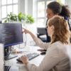 Two professional women discussing code on a computer screen.