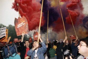protesters holding signs with flare smoke in background