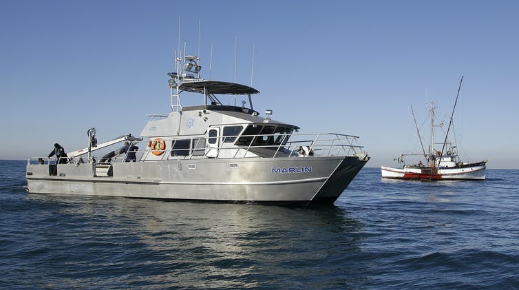 A California game warden boat next to a fishing boat.