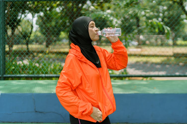 woman in hijab drinks water after sport