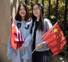 two women with U.S. and China flags, one wearing a graduation gown