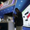 A woman looks at her phone while standing in a tradeshow booth that has a display in Chinese.