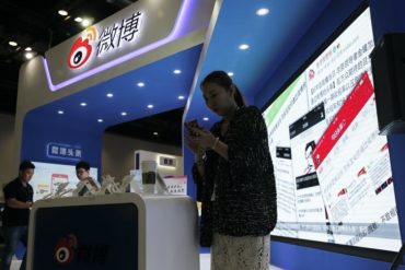 A woman looks at her phone while standing in a tradeshow booth that has a display in Chinese.