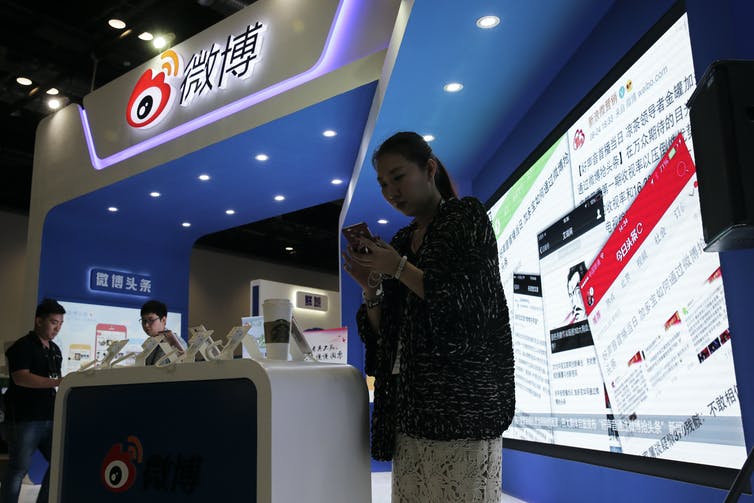 A woman looks at her phone while standing in a tradeshow booth that has a display in Chinese.