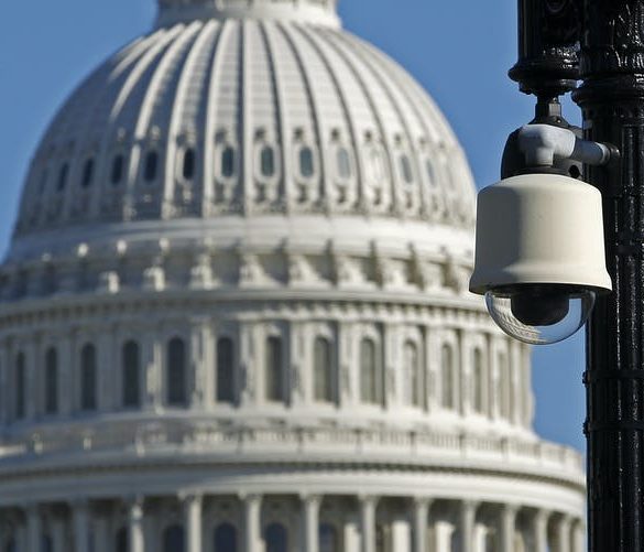 A security camera mounted on a streetlight pole with the U.S. Capitol dome in the background