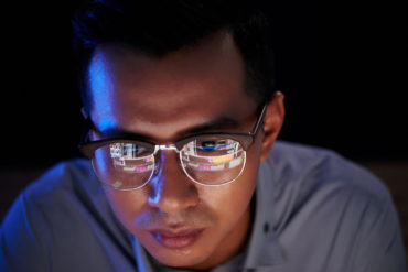 Software developer with programming code reflecting in his glasses