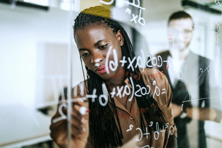 Black woman writing formulas on a board.
