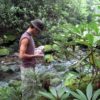 Man holding plastic bottles stands in stream.