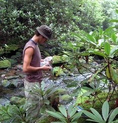 Man holding plastic bottles stands in stream.