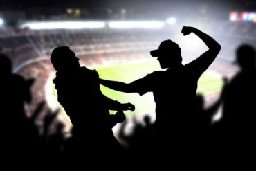 Fight in a football game crowd. Angry man hitting another spectator in soccer match audience. Violent argument between two fans of different teams and clubs.