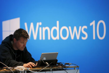 A man works on a laptop computer near a Windows 10 display at Microsoft Build in San Francisco