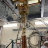 The HAYSTAC detector, a large copper cylinder connected to a gold-plated assembly of tubes and wires hanging from the ceiling of a lab.