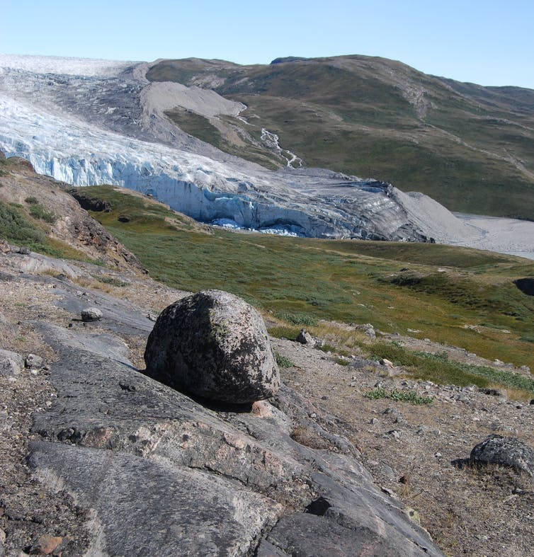 A rock and tundra with a glacier in the background