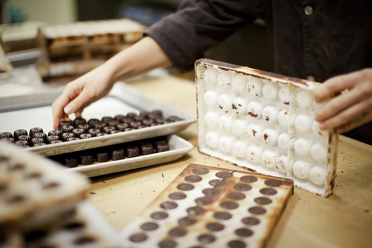 a chocolate maker's hands remove finished candies from a chocolate mold