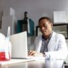 man in white coat in lab at laptop