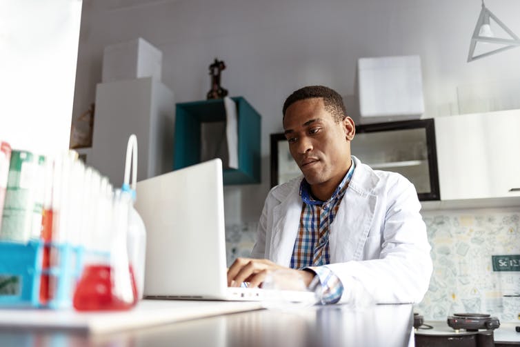 man in white coat in lab at laptop