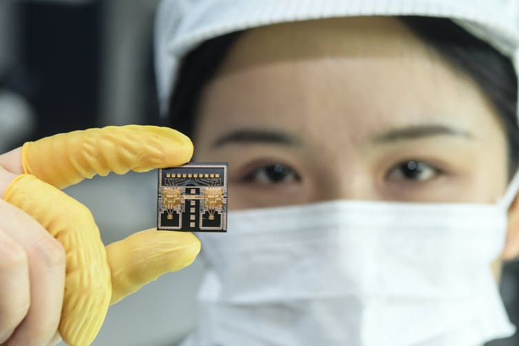 a worker wearing a facemask and finger gloves holds a semiconductor chip