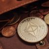 A commemorative coin bearing a double-pyramid logo lies in an open leather wallet containing euro coins