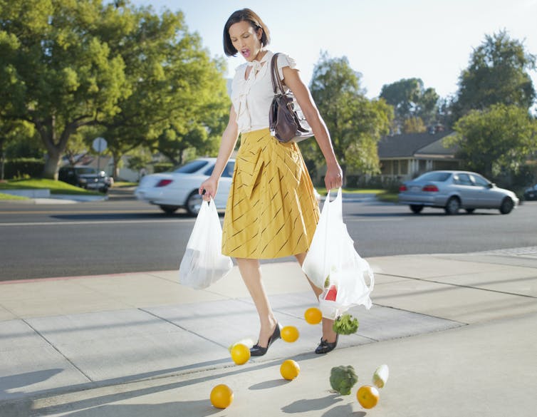woman with fruit spilling out of ripped grocery bags