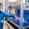 woman in PPE inserts specimens into lab equipment