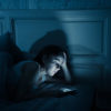 Young attractive woman awake late at night using smart phone lying in bed in a dark bedroom. Using mobile for chatting and sending messages in internet addiction, mobile abuse and insomnia concept