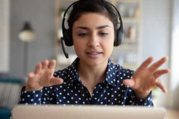 Woman wearing wireless headset video conference calling on laptop