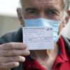 masked older man holds up his vaccination card