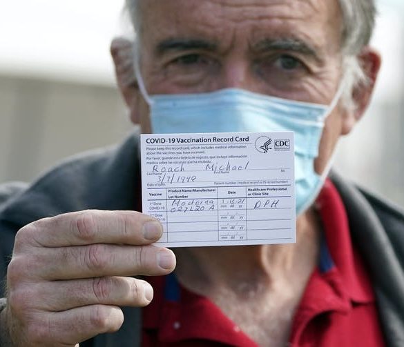 masked older man holds up his vaccination card