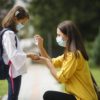 masked mother helps masked daughter in backpack with hand sanitizer