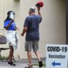 man removes hat for temperature check at COVID-19 vaccination site