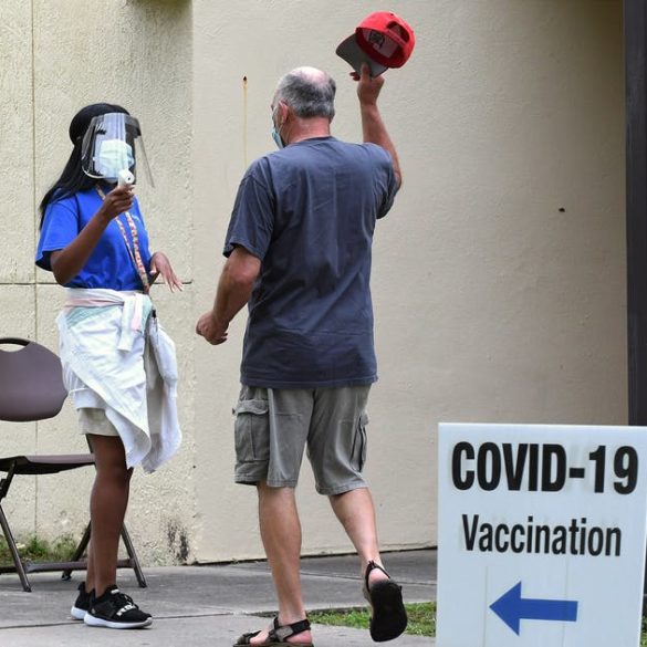 man removes hat for temperature check at COVID-19 vaccination site