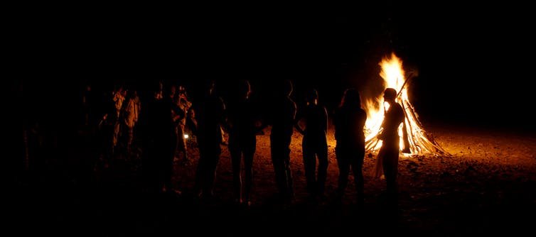 people silhouetted against bonfire at night