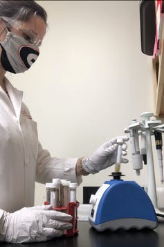masked scientist holding various test tubes