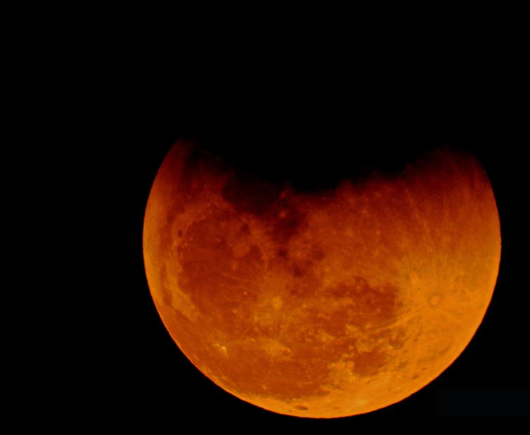 A red hued moon with a shadow on the top.