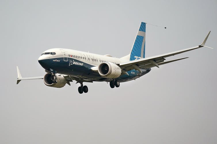 A twin-engine jetliner with its landing gear partway down and the name Boeing on the side descends through the air