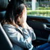 woman in a car's driver's seat covers her face with her hands