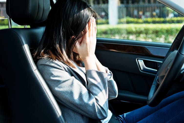 woman in a car's driver's seat covers her face with her hands