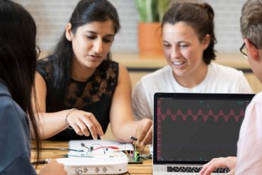 Students at a table use a Moku Go device to test a circuit board.
