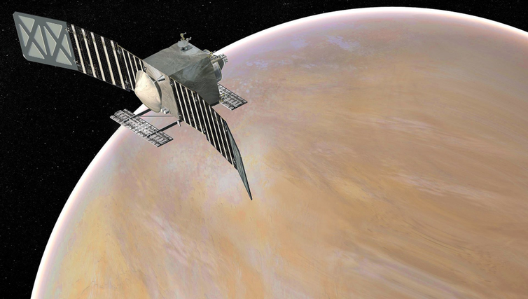 A square satellite with two long solar panels above a tan–colored Venus.