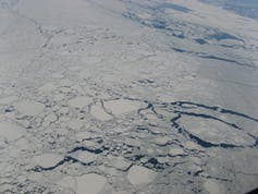 An aerial photo of pack ice with large block of ice floating on the sea and small cracks showing water between chunks of ice.