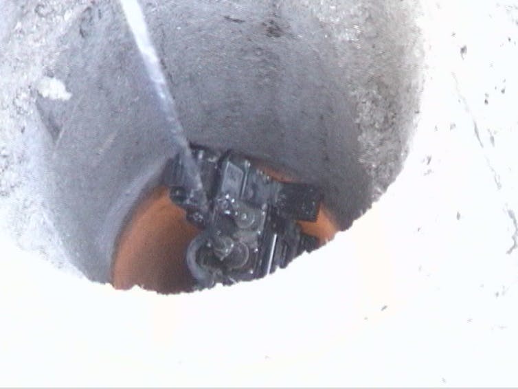 A cable attached to a piece of equipment inside a round hole in a concrete surface