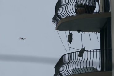 to the left a drone is in the air, to the right are two balconies of an apartment building tower