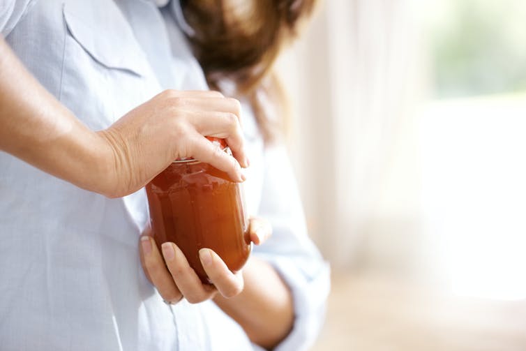 A woman struggling to open a jar full of preserves.