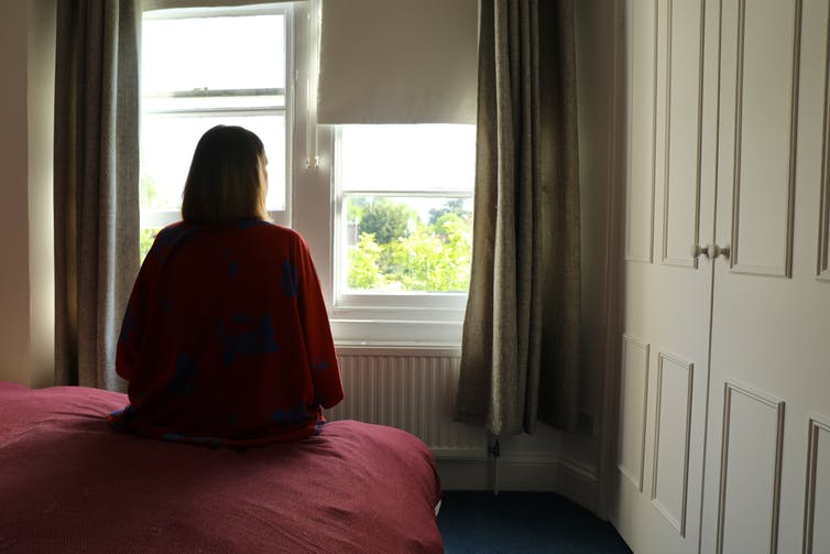 view from behind of woman sitting on bed and looking out window