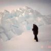 A person standing on an ice chunk with a large ridge of ice in front of them.