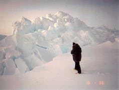 A person standing on an ice chunk with a large ridge of ice in front of them.